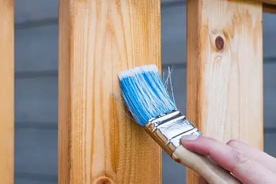 PaintMor Painters professional fence painting and staining, image of a painter's hand applying stain to a wood fence in Little Elm.