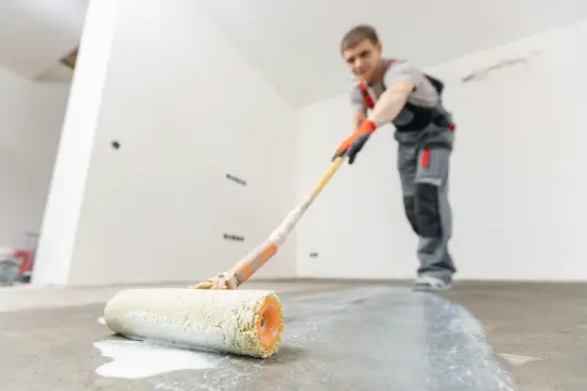 PaintMor Painters professional garage floor epoxy and painting services in Little Elm, showing a painter applying grey epoxy on a garage floor.