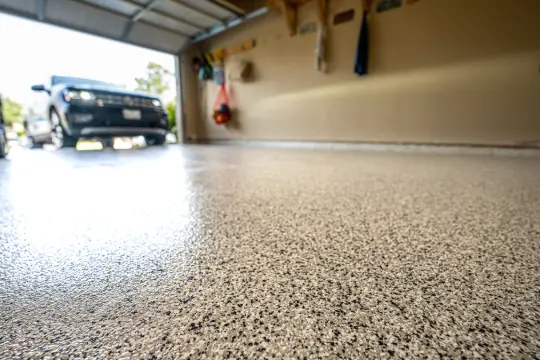 PaintMor Painters professional garage floor epoxy and painting services in Richardson, showing a tan speckled glossy epoxy on a garage floor with a black car.