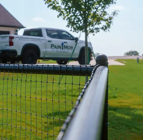 PaintMor Painters professional fence painting and staining, image of black painted metal fence with PaintMor Painters truck in the background.